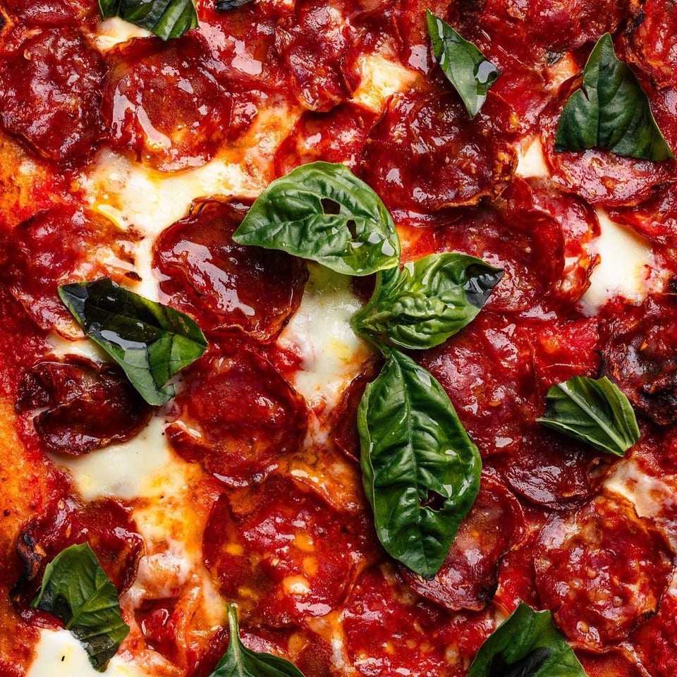 Close-up of a Mille Luci Pizzeria pepperoni pizza with melted cheese, red sauce, and fresh basil leaves.