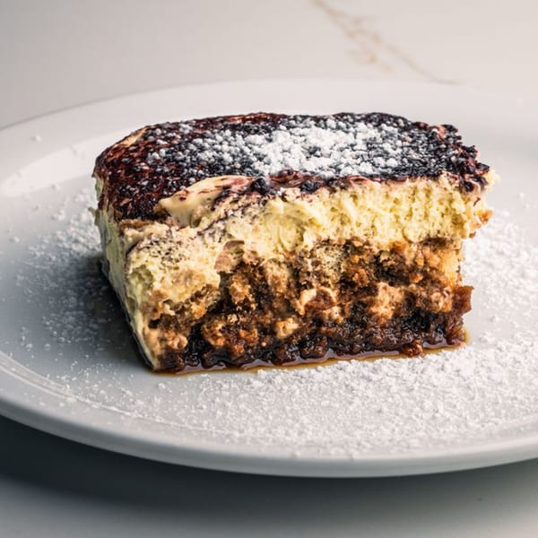 A slice of Mille Luci Pizzeria's tiramisu, dusted with powdered sugar and cocoa, on a white plate.