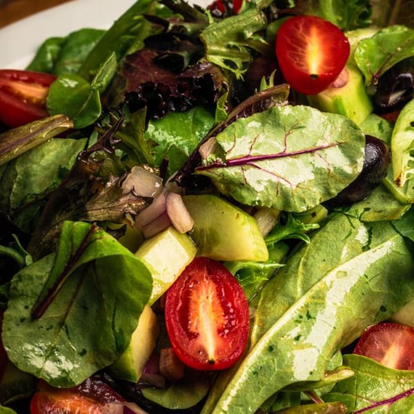 Close-up of a vibrant green salad with halved cherry tomatoes and avocado chunks.