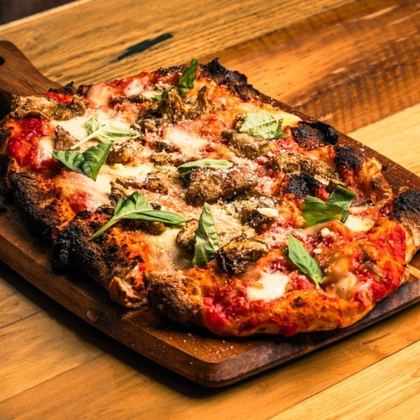 Mille Luci Pizzeria's rectangular pizza with sausage, cheese, tomato sauce, and basil on a wooden board.