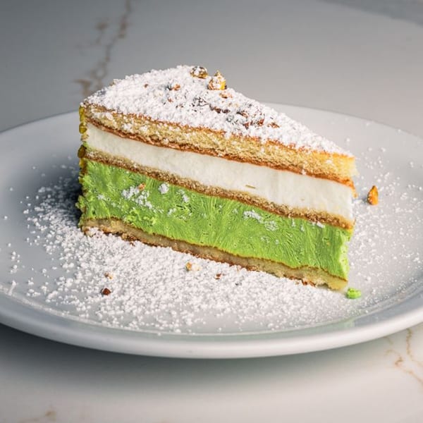 A slice of Mille Luci Pizzeria's layered cake with green and white filling, dusted with powdered sugar.
