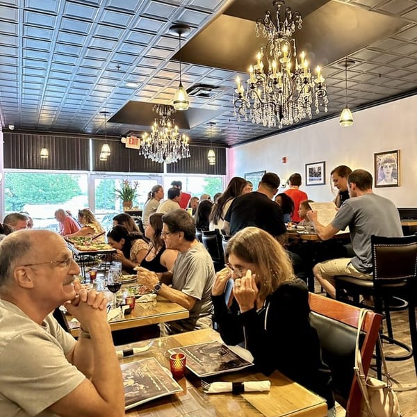 Diners enjoying pizza and drinks in the lively, chandelier-lit Mille Luci Pizzeria dining room.