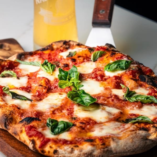 Mille Luci Pizzeria's Margherita pizza with fresh basil, mozzarella, and tomato sauce, next to a beer.