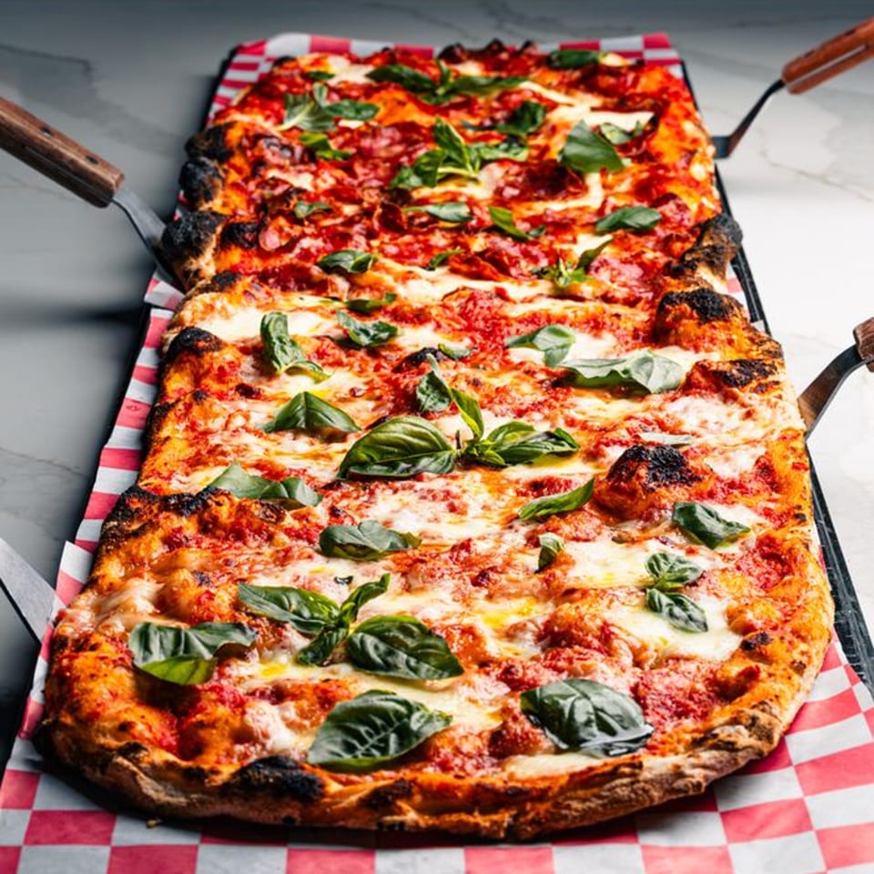Two rectangular Mille Luci Pizzeria pizzas with melted cheese, red sauce, and fresh basil on checkered paper.